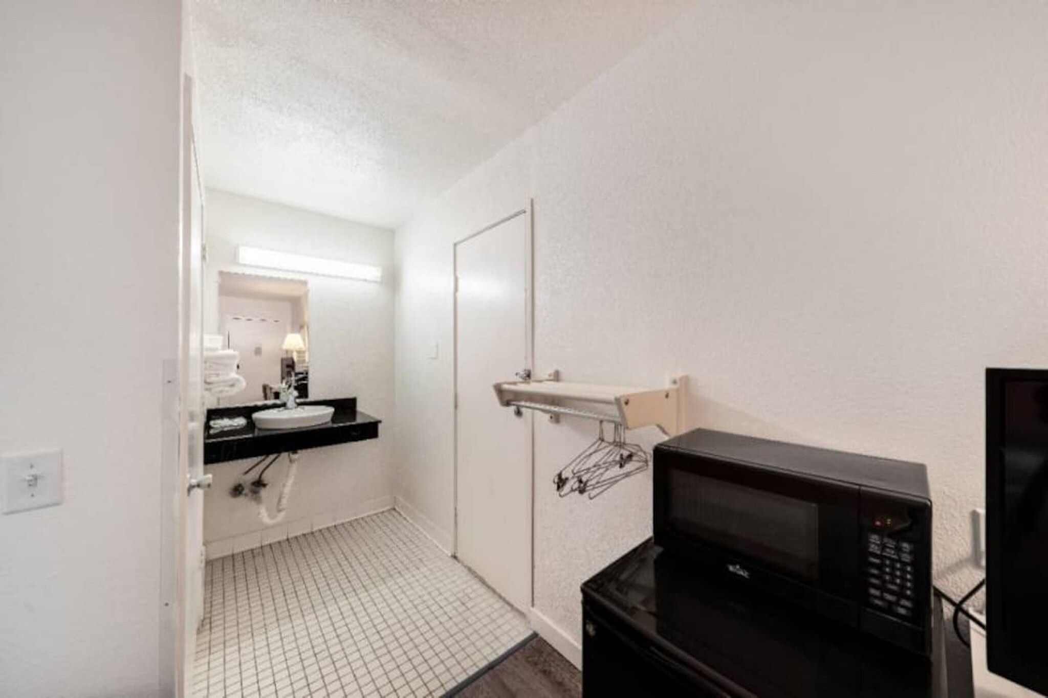 A hotel bathroom with a sink, mirror, towel rack, and a microwave.