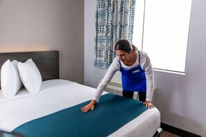 Une chambre d’hôtel avec un lit bien fait, une fenêtre avec des rideaux et un mur orné d’un motif géométrique.