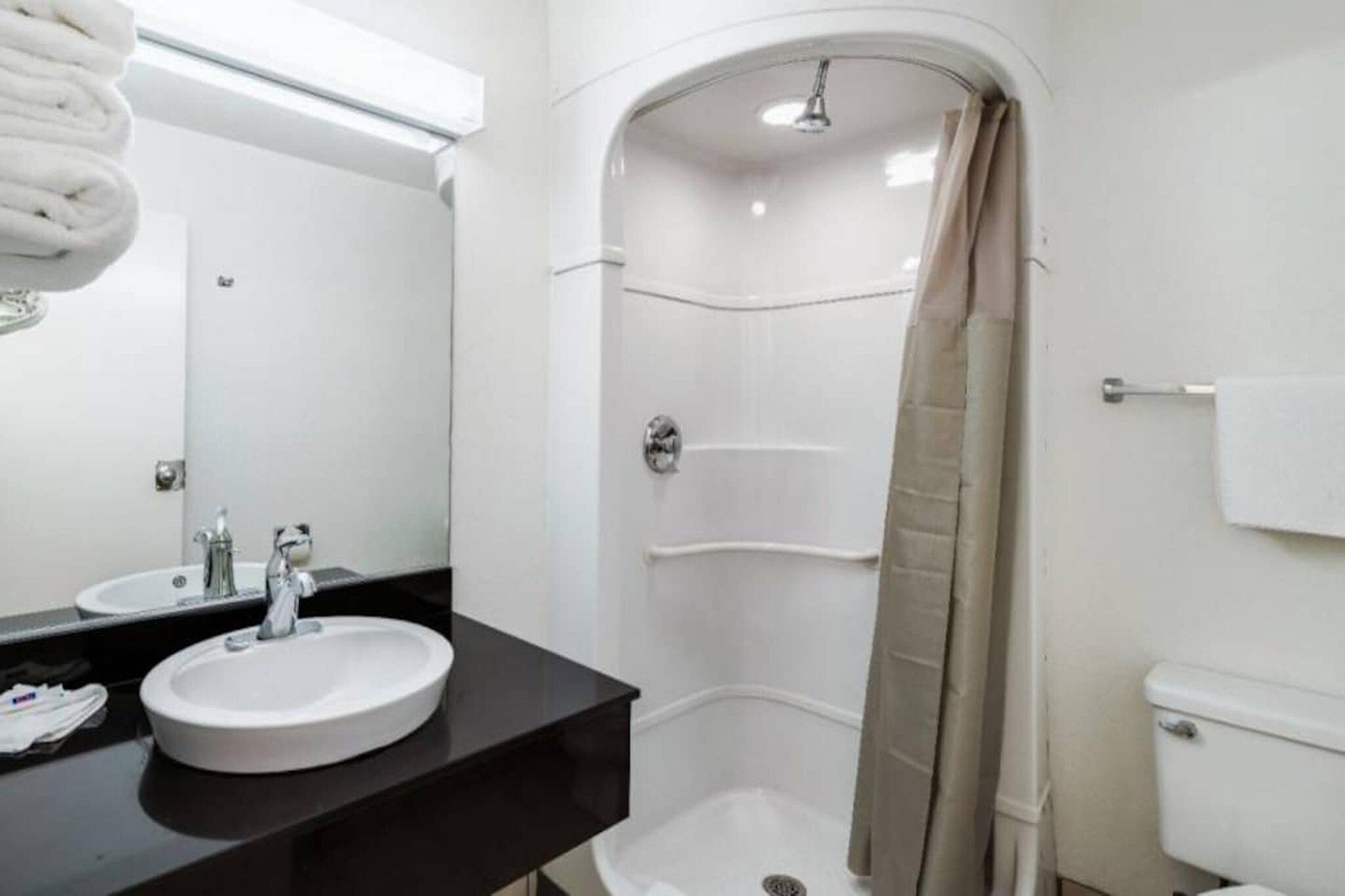 A modern bathroom with a round sink, a mirror, a shower with a beige curtain, and a toilet.