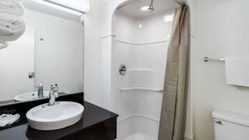 A modern bathroom with a round sink, a mirror, a shower with a beige curtain, and a toilet.