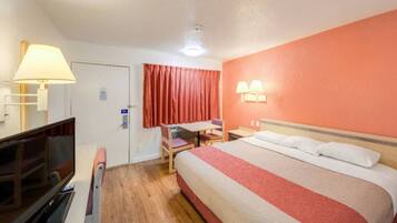 A hotel room with a bed, a desk, a chair, a television, and a lamp.