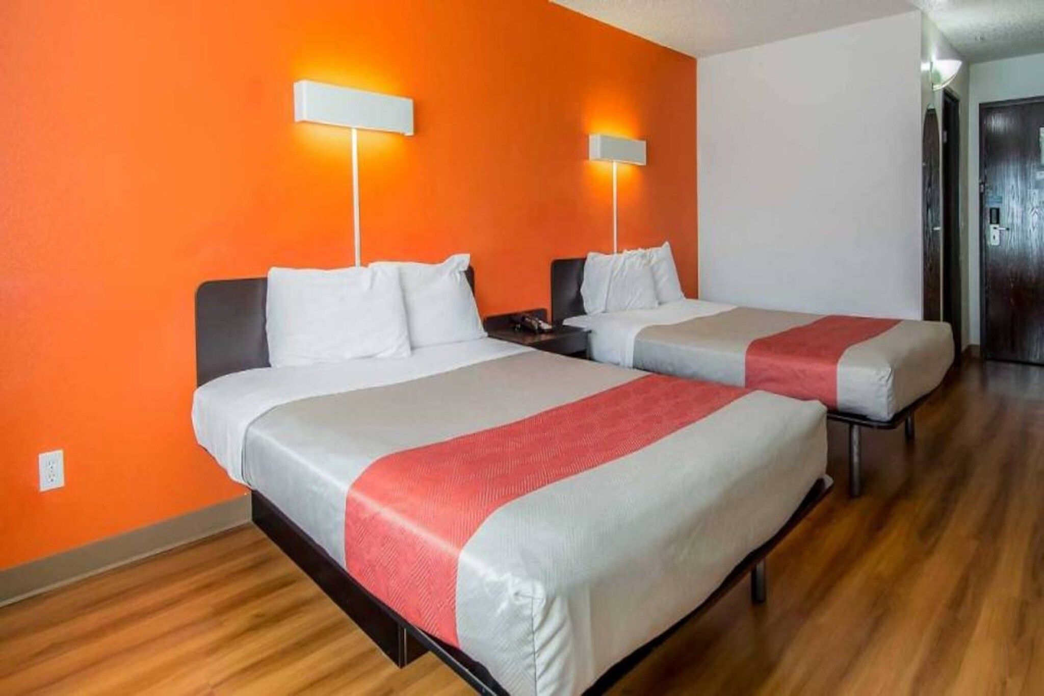 A hotel room with two beds, each with white bedding and a red accent.