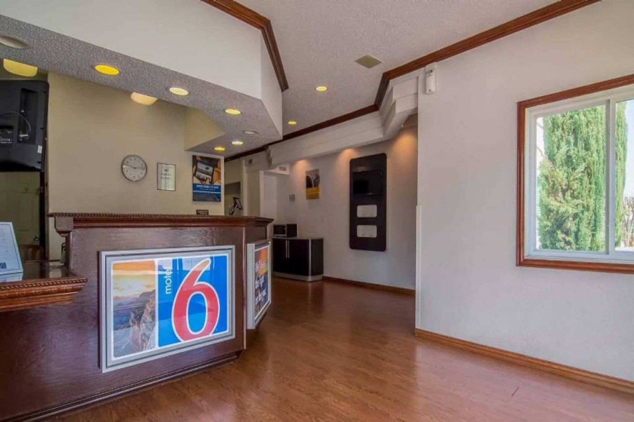 A reception area with a wooden reception desk, a clock, and a window with a view of trees.