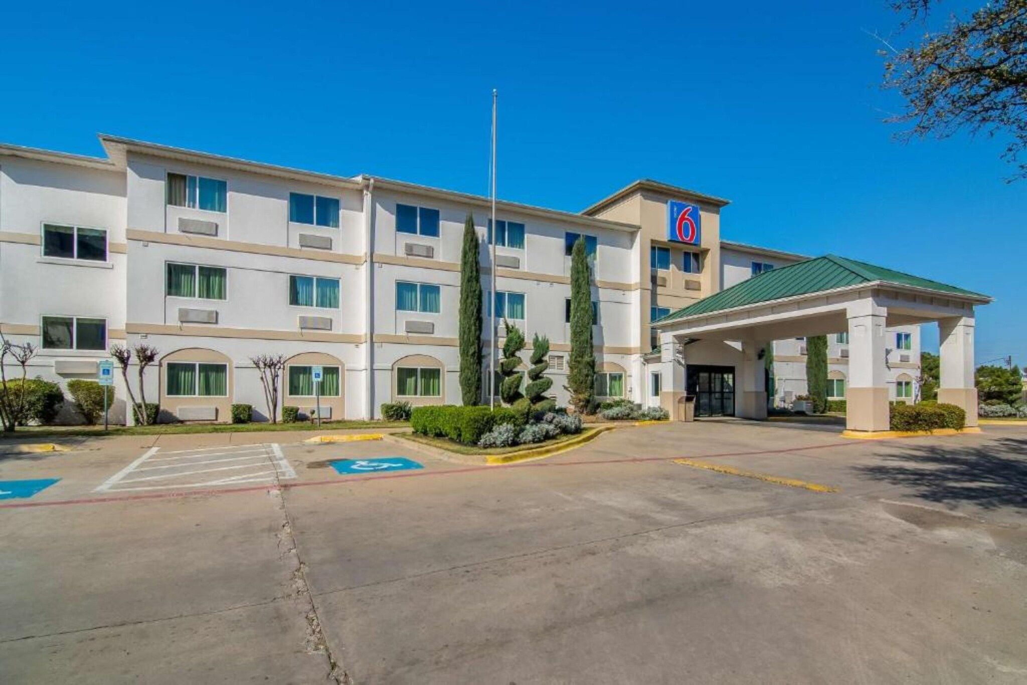 A multi-story hotel with a parking lot, a covered entrance, and a sign indicating the hotel name.