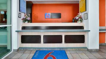 A hotel reception desk with a blue carpet featuring a red number 6, a sign with the number 6, and a flower arrangement on the counter.