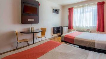 A hotel room with two beds, a desk, a chair, a television, and a window with curtains.
