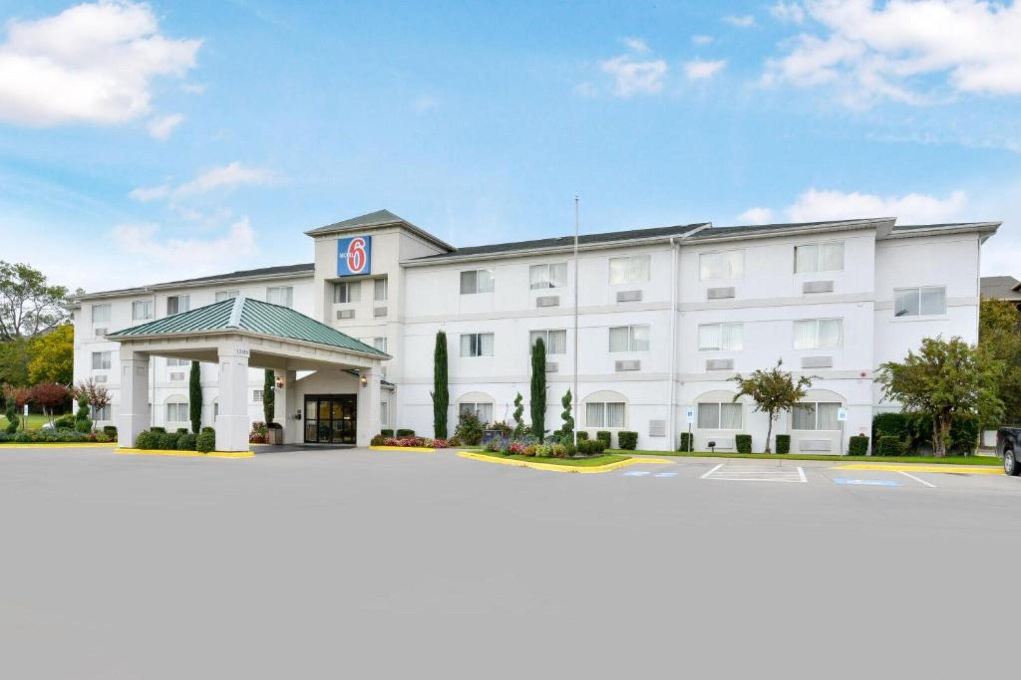 A multi-story hotel with a central entrance, a covered parking area, and a clear sky.