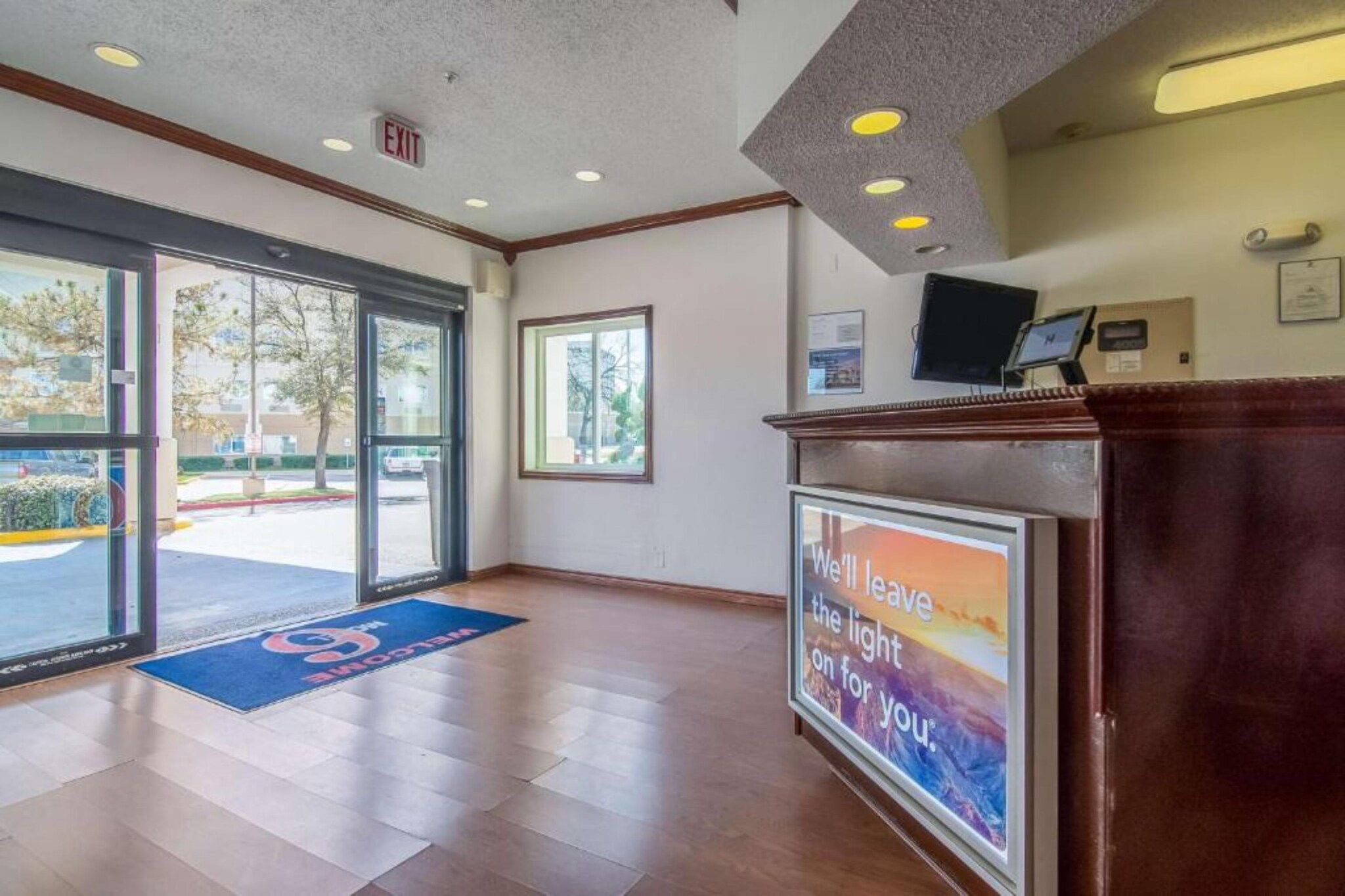 A hotel reception area with a glass door entrance, a reception desk, and a poster on the wall.