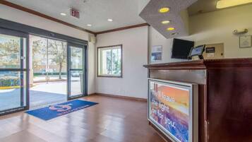 A hotel reception area with a glass door entrance, a reception desk, and a poster on the wall.