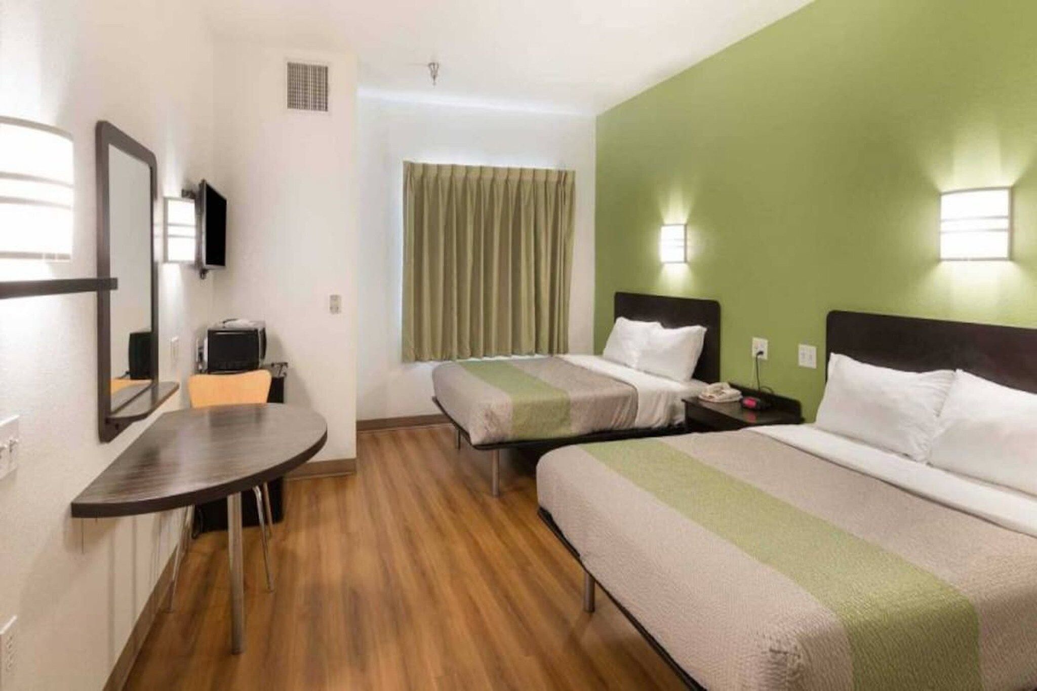 Habitación de hotel con dos camas, un escritorio, una silla, un televisor y una ventana con cortinas.