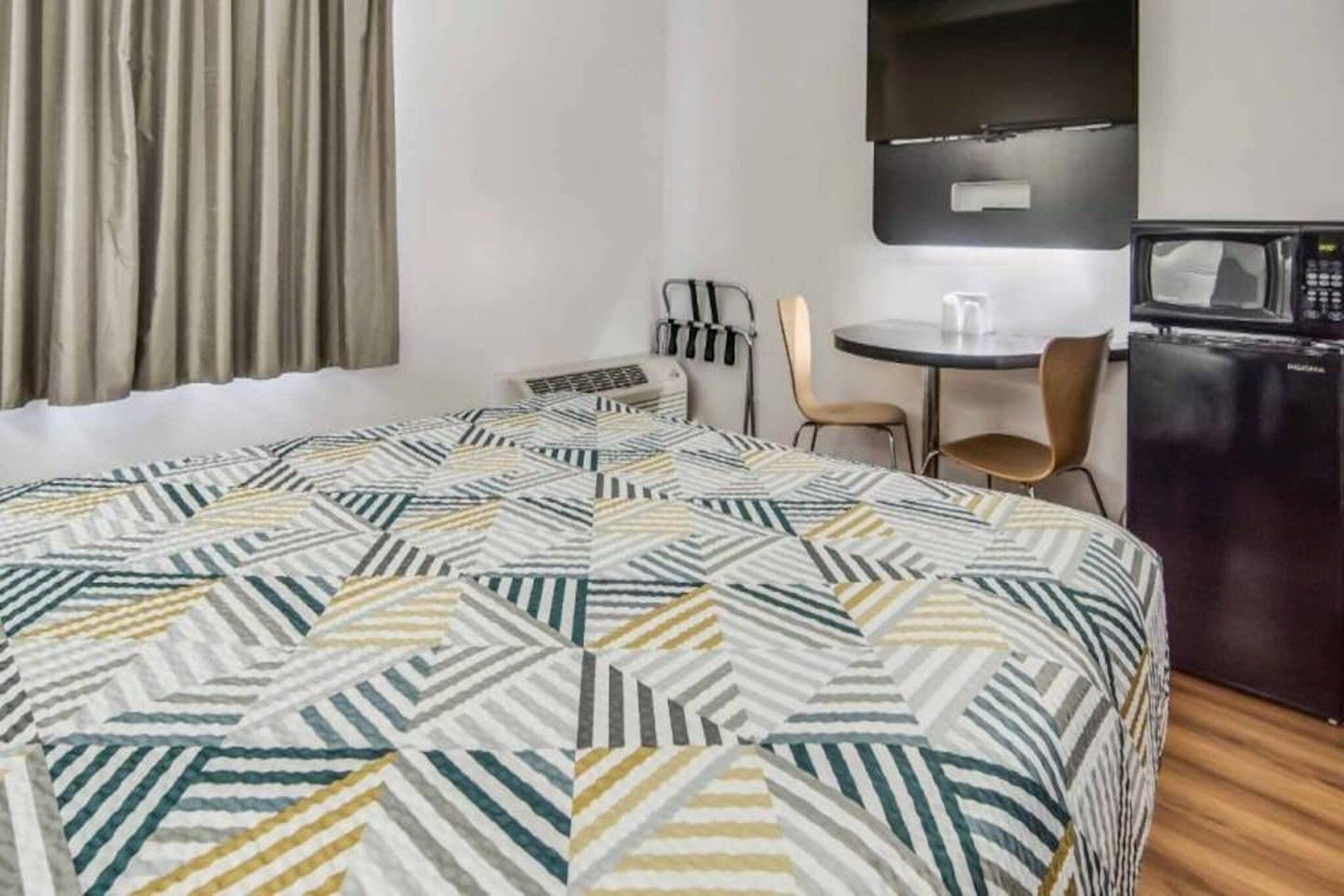 A hotel room with a bed, a desk, a chair, a microwave, and a refrigerator.