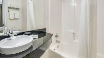 Een badkamer met een wit wastafel, een spiegel, een douche en een bad.