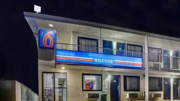 A motel with a '6' sign, a 'WELCOME' sign, and a balcony.