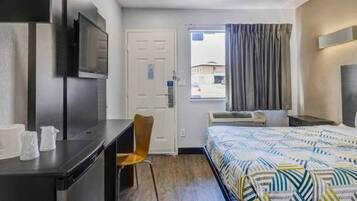 A hotel room with a bed, a desk, a chair, a TV, a window with curtains, and an air conditioning unit.