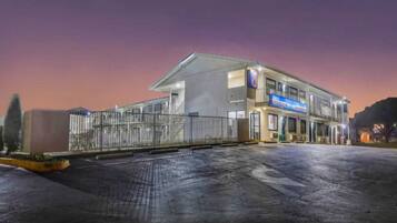 A multi-story building with a flat roof, a gated entrance, and a parking area.