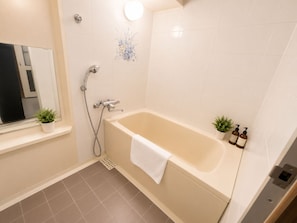 A bathroom with a bathtub, a shower, a mirror, and two potted plants. - Ocean Shinsaibashi Higashi (Osaka)
