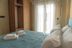 A hotel room with a bed, a wooden wardrobe, and a window with curtains. - Amnia Villas, Be on Holidays (Rethymno)