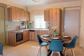 A modern kitchen with wooden cabinets, a microwave, and a dishwasher. There is a dining table with chairs and a vase of flowers. - Amnia Villas, Be on Holidays (Rethymno)