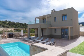 A modern two-story building with a pool, outdoor seating, and a barbecue area. - Amnia Villas, Be on Holidays (Rethymno)