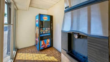 A vending machine with a Nestle logo, located in a corner with a tiled floor and a window to the left.