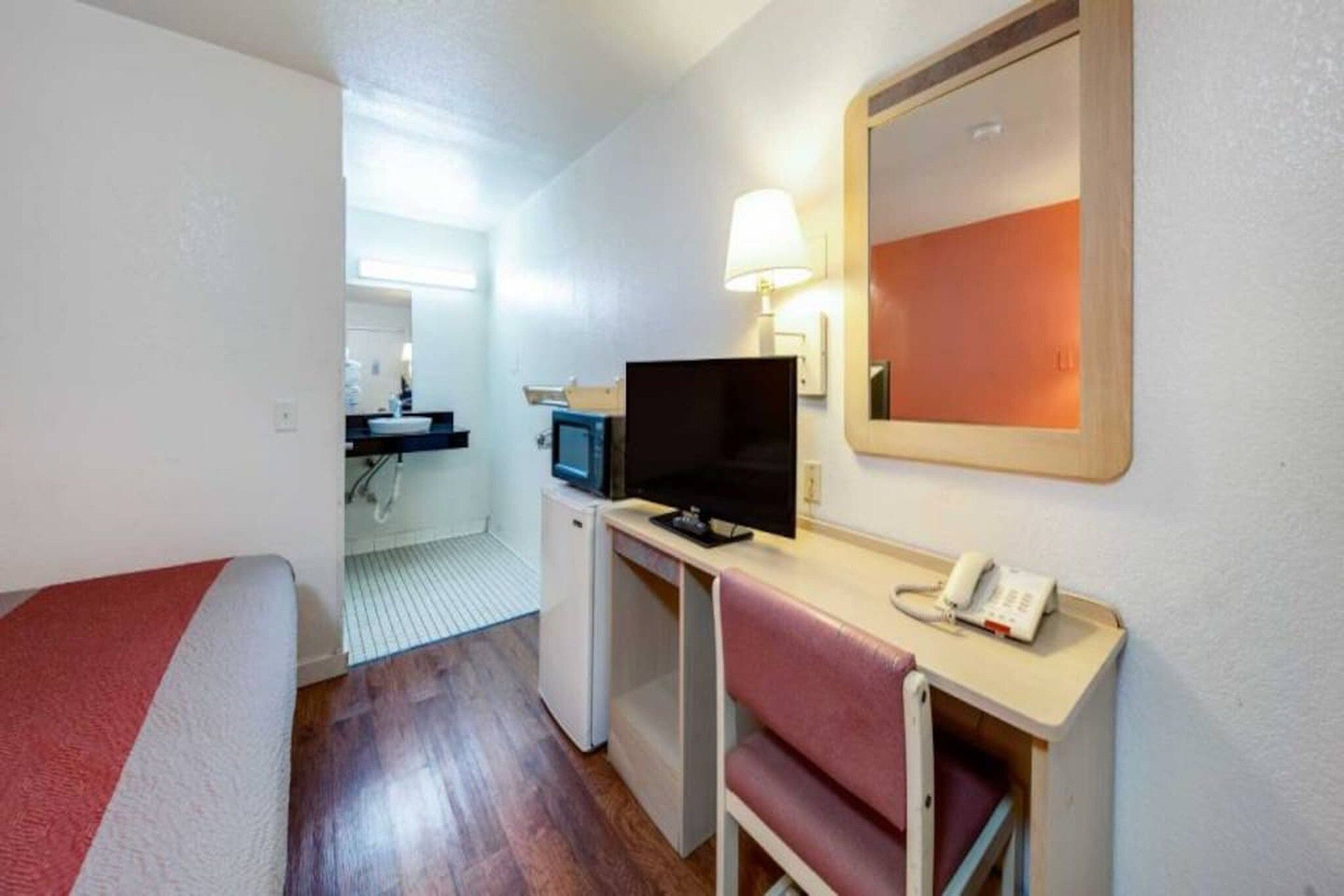 A hotel room with a bed, desk, chair, television, and a telephone.