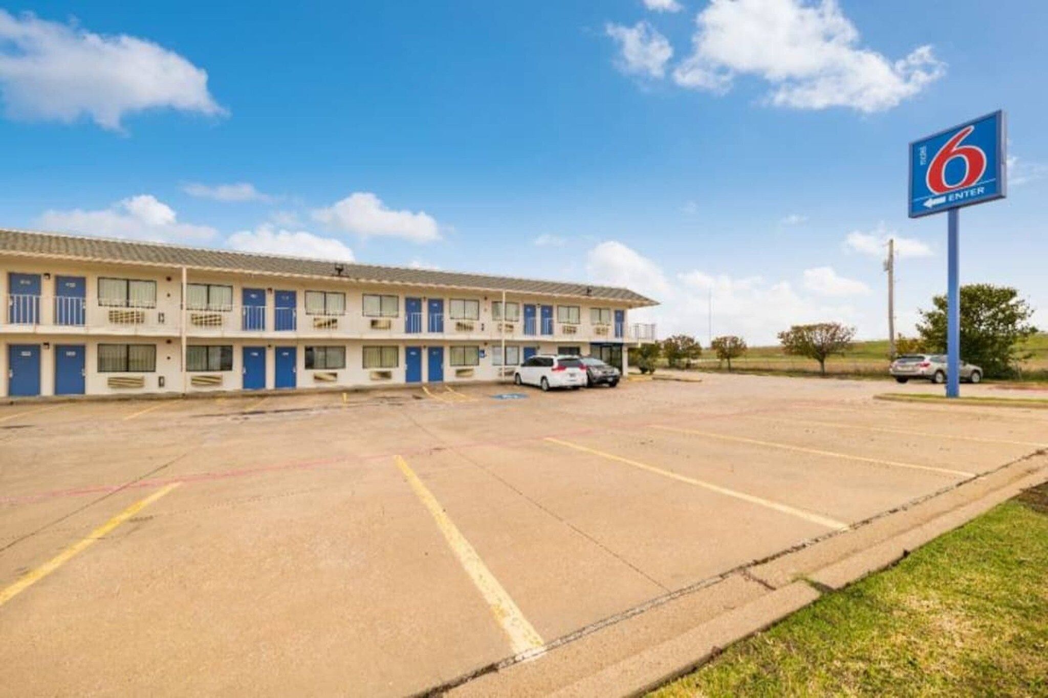 Un motel con varias habitaciones, estacionamiento y cielo despejado.