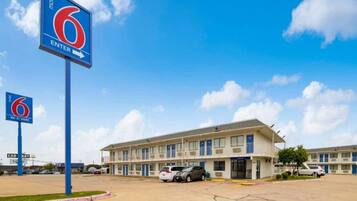 A motel with a large building, multiple parking spaces, and a clear sky.