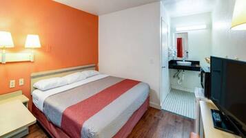 A hotel room with a bed, bedside lamps, a desk with a computer, and a television.