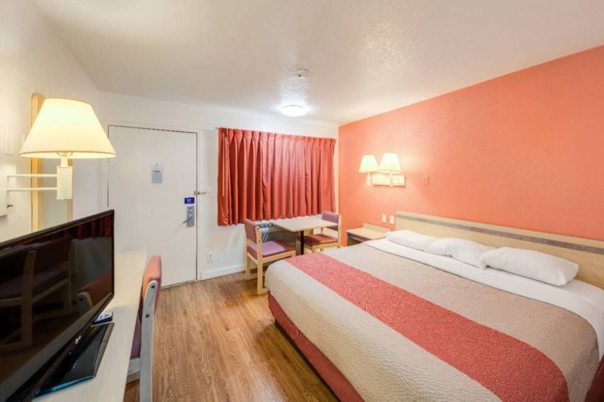 Una habitación de hotel con cama, escritorio, silla, televisor y lámpara.