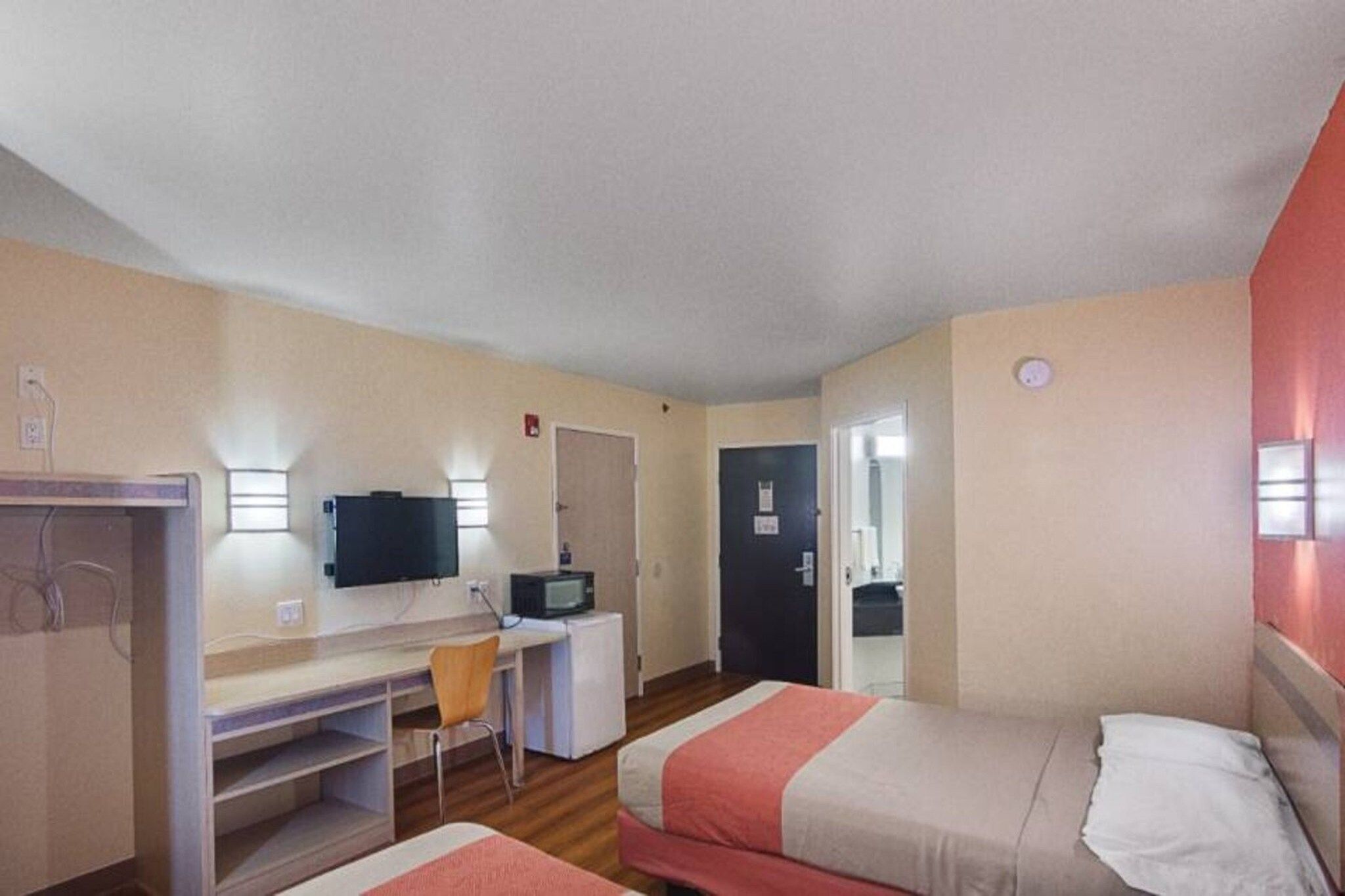 Een hotelkamer met een bureau, twee bedden, een stoel en een televisie.