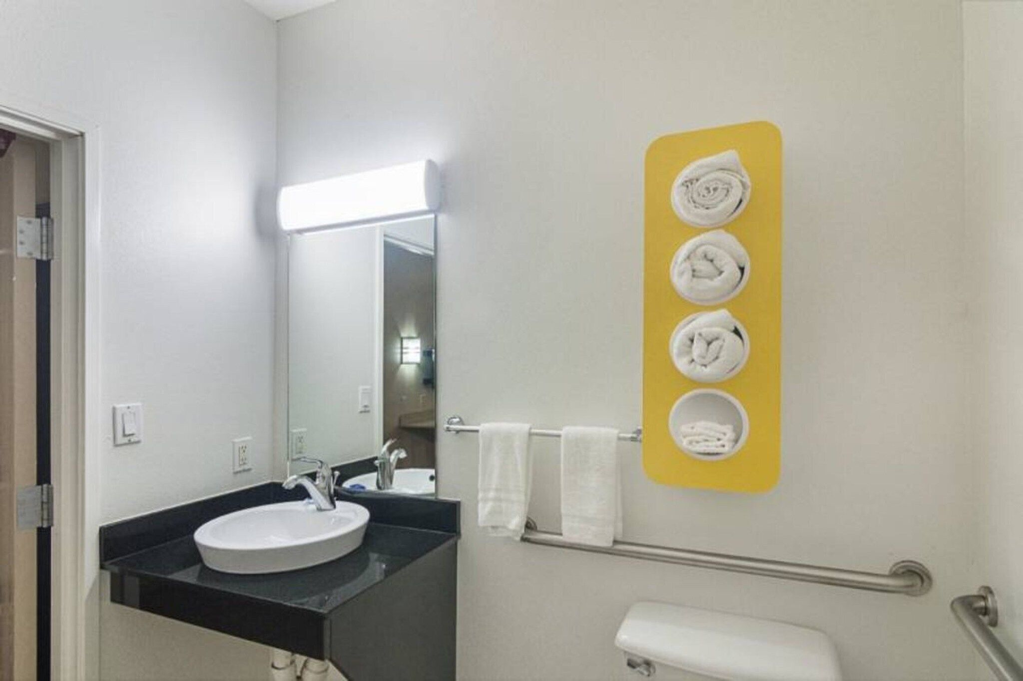 Un baño con lavamanos, espejo, toallero y barandilla.