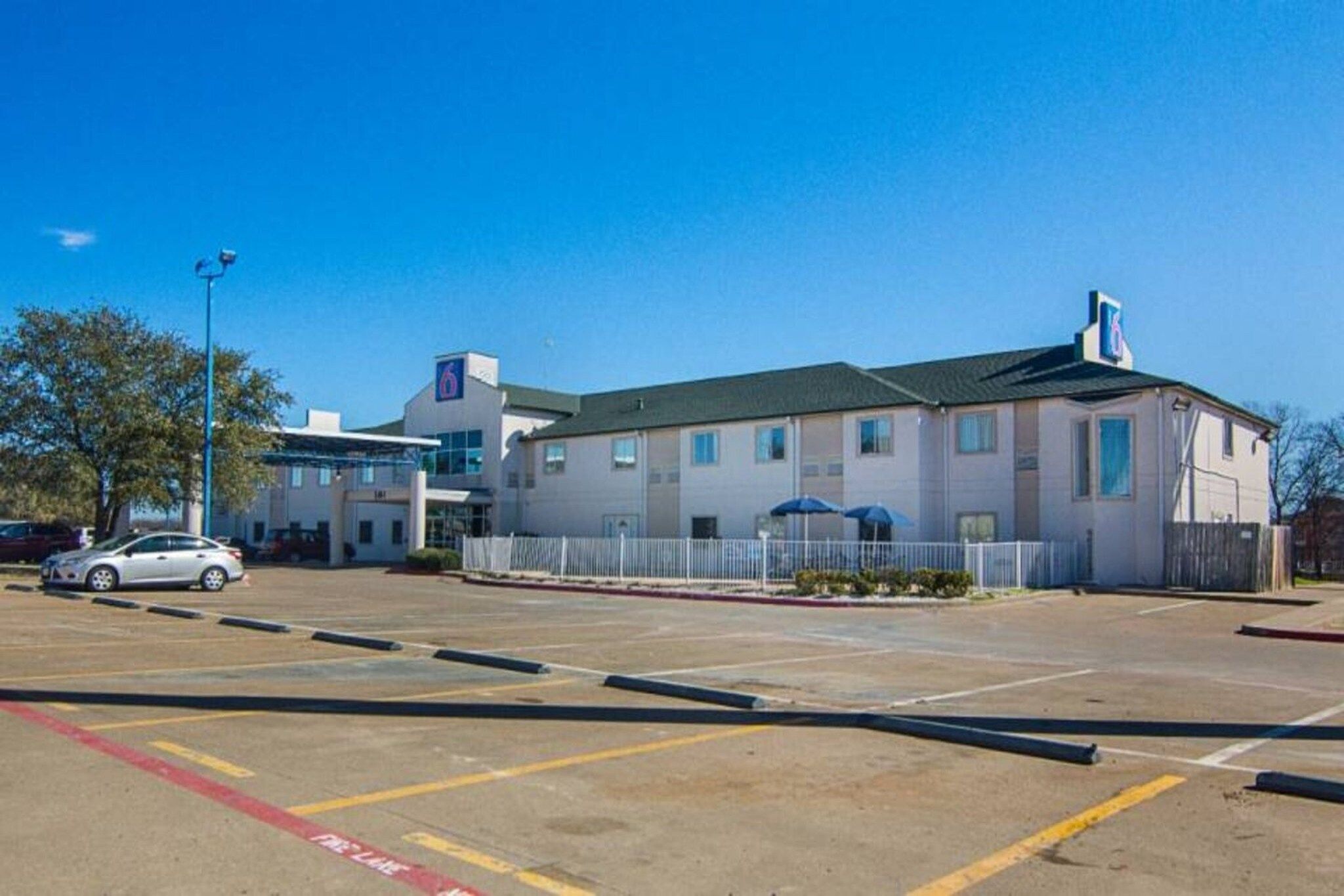 A parking lot with a building that has a flat roof and a sign with a blue and white logo.