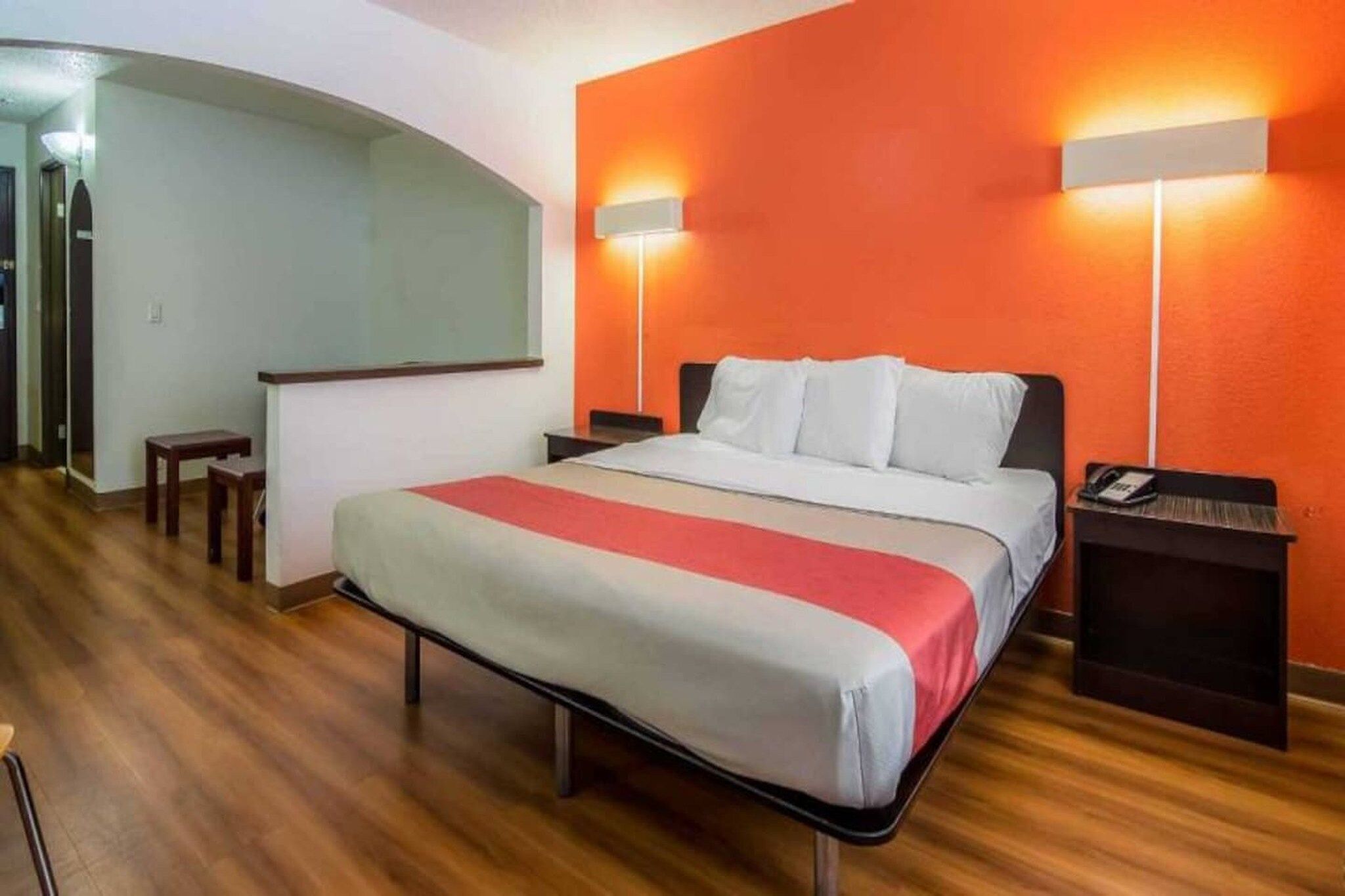 A hotel room with a bed, a nightstand, a lamp, and a wall-mounted light fixture.