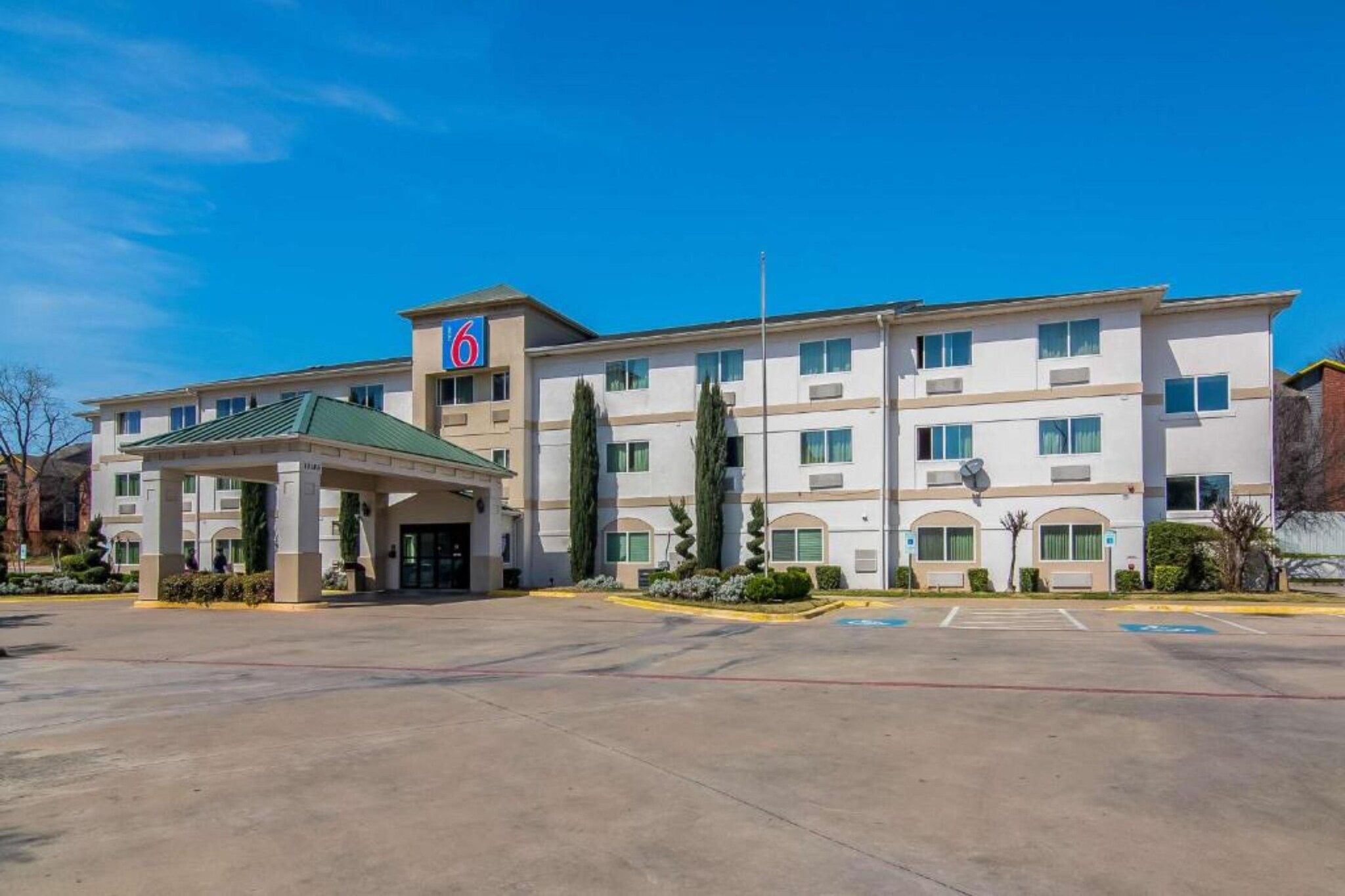 A multi-story hotel with a flat roof, a covered entrance, and a parking lot.