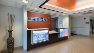 A reception desk with a digital screen displaying a message, a clock, and framed pictures on the wall.