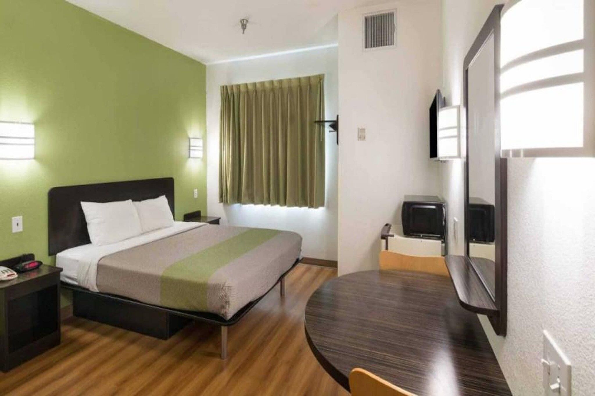 Una habitación de hotel con una cama, mesita de noche, una silla y un escritorio pequeño con otra silla.