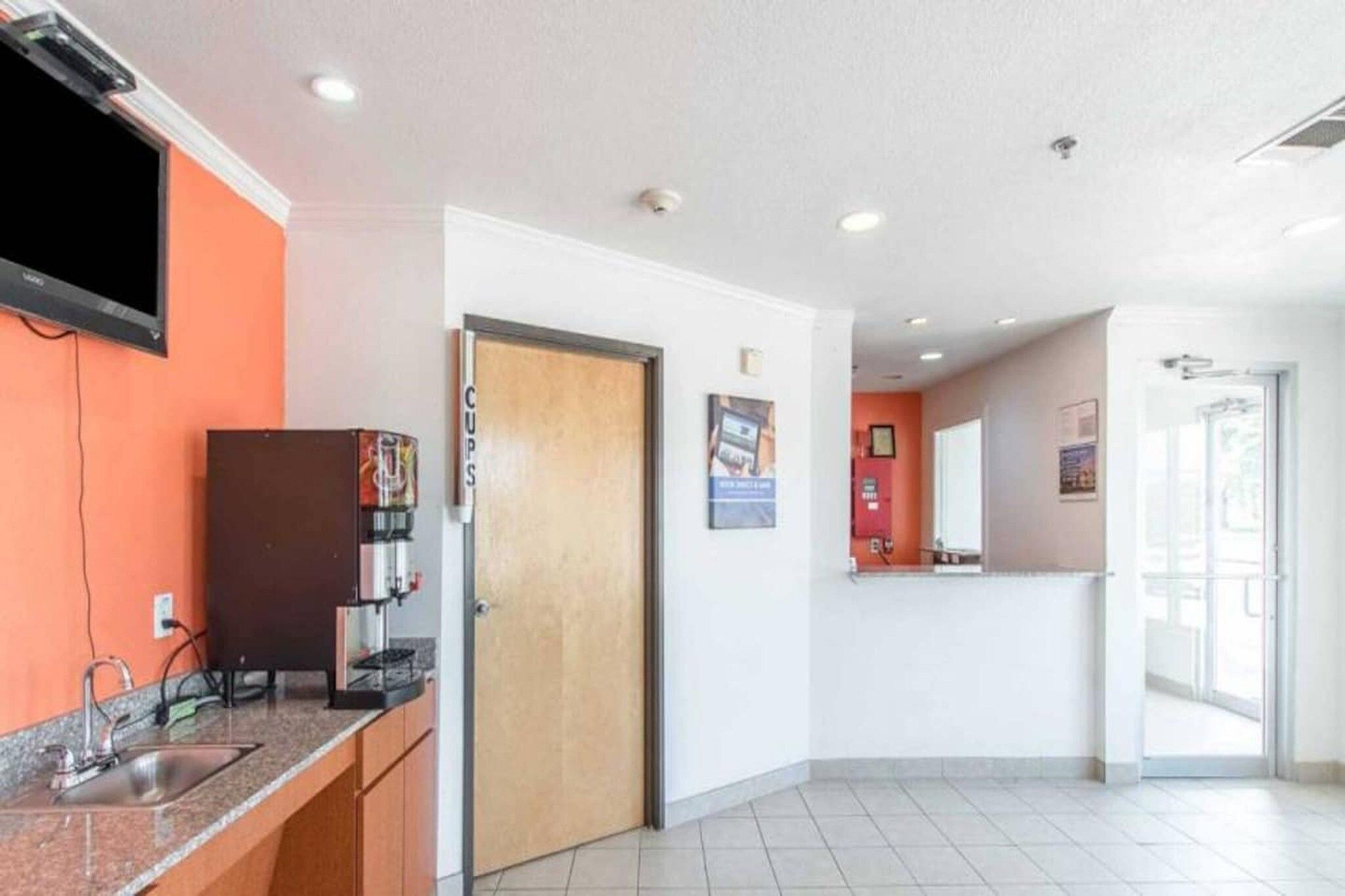 A hotel lobby with a reception desk, a coffee machine, and a door leading to a room.