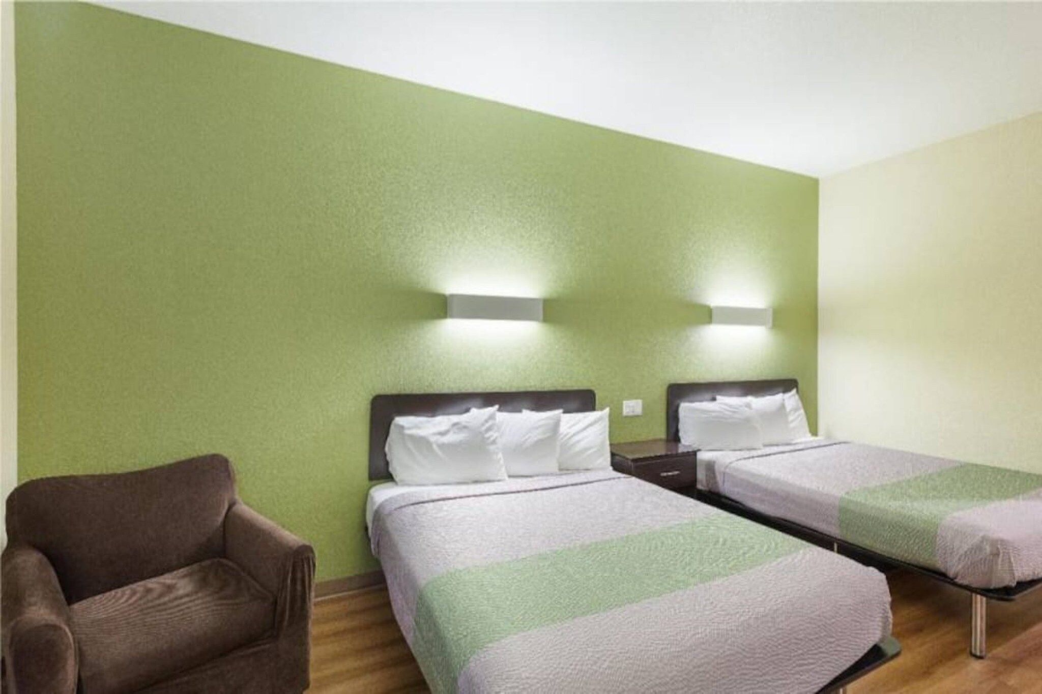 A room with two beds, a chair, and two wall-mounted lights.