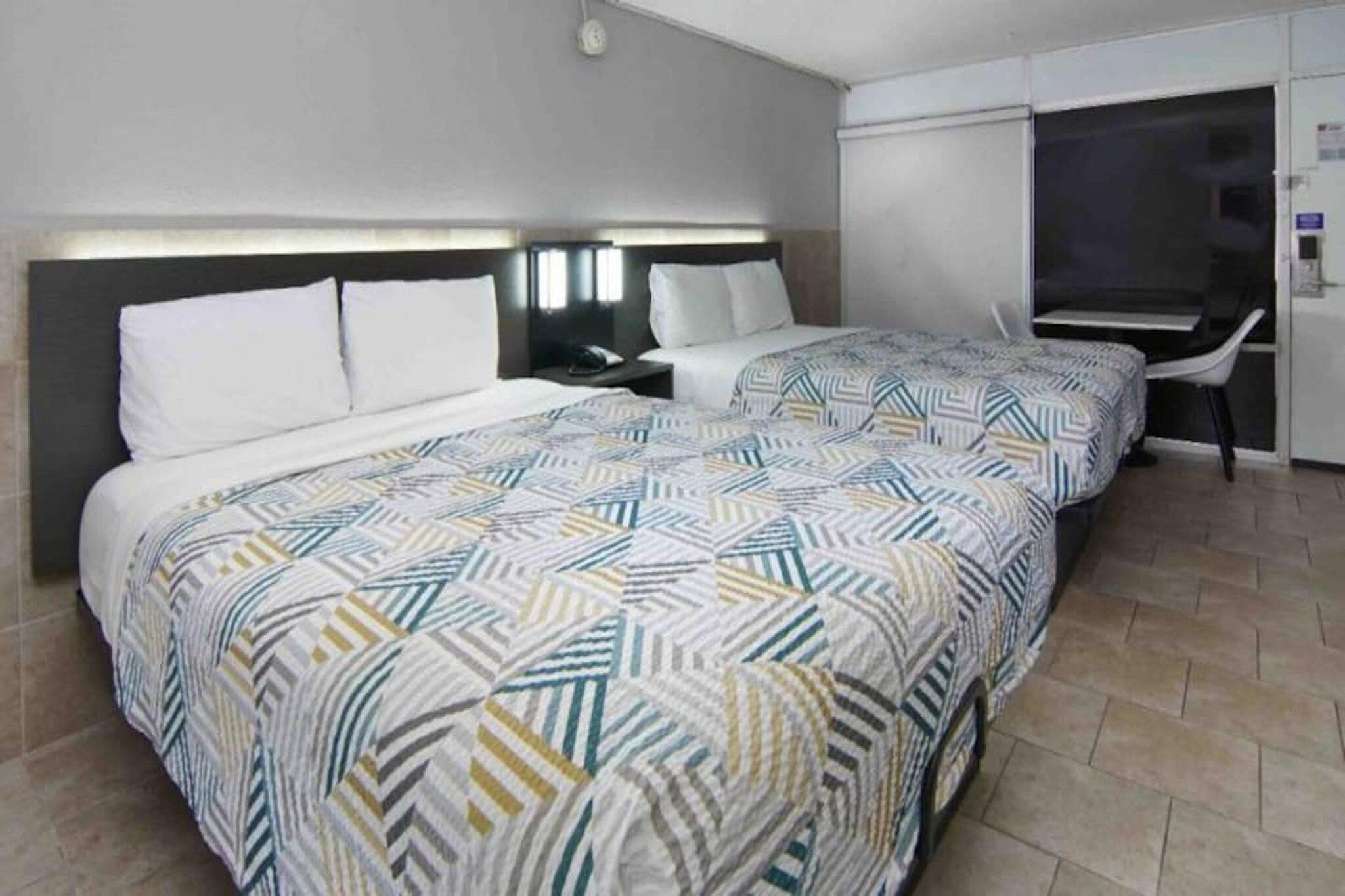 A hotel room with two beds, a desk, and a chair.