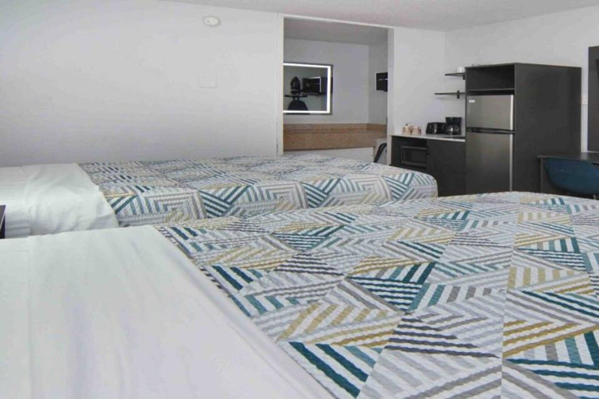 A hotel room with two beds, a kitchenette, and a mirror.