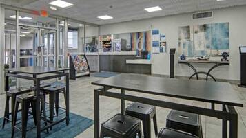 A modern interior with tables and stools, a bulletin board, and a counter.