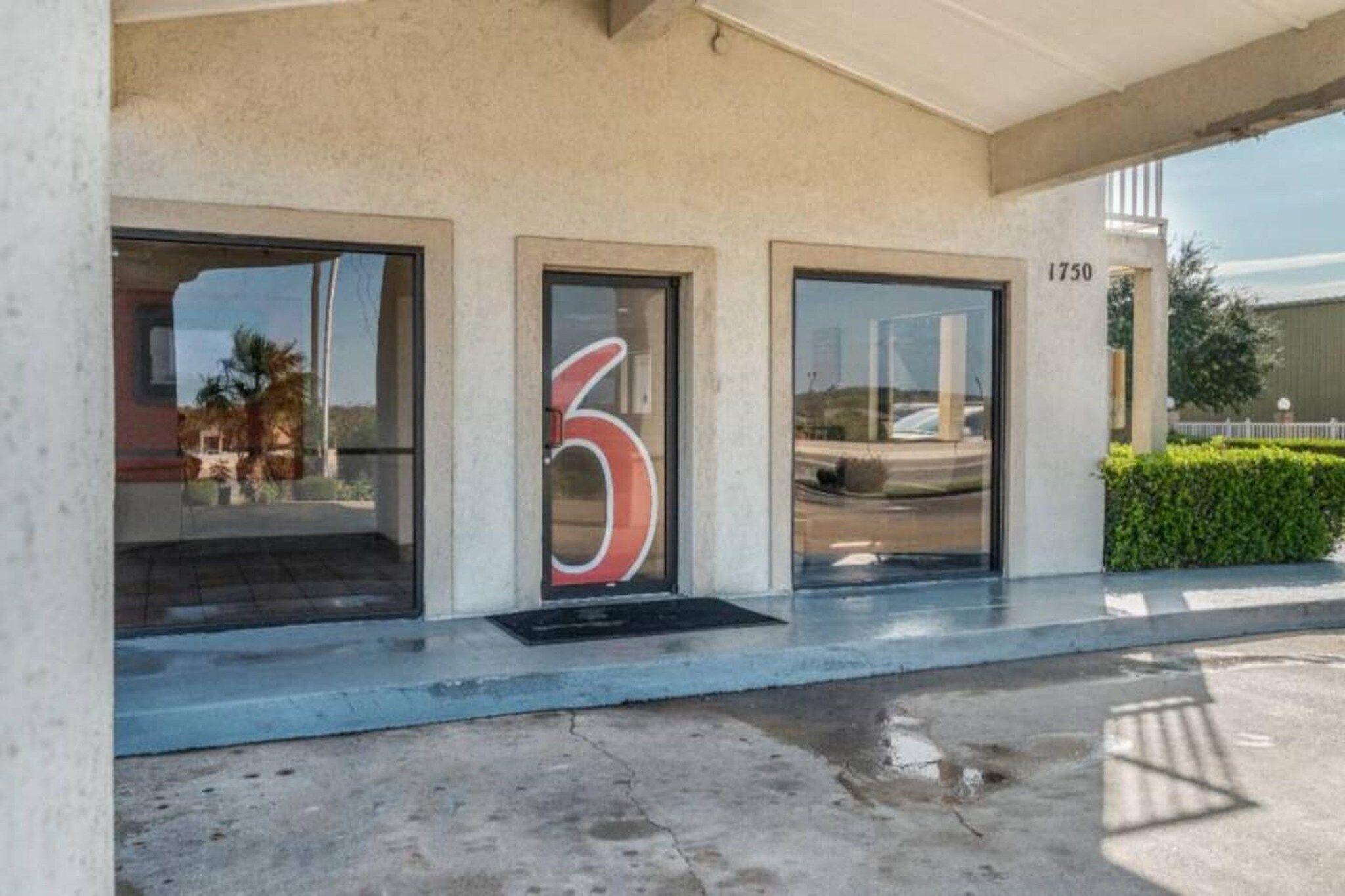 A building entrance with a large number '6' on the door, a concrete ramp leading up to the entrance, and a street view visible through the windows.