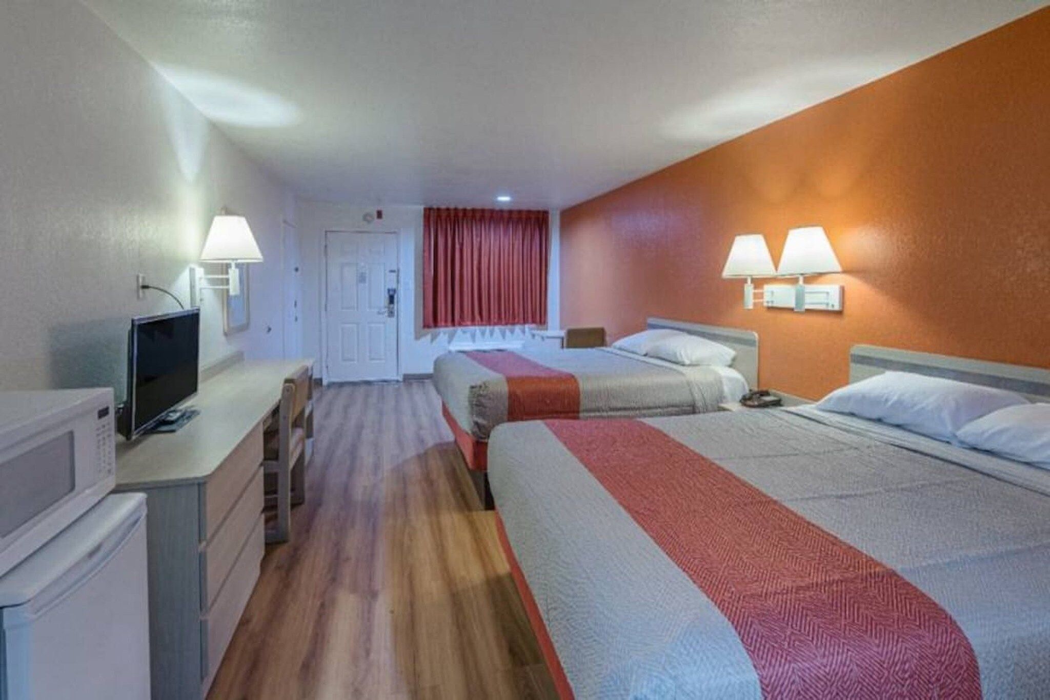 A hotel room with a bed, a desk, a television, and a door leading to another room.