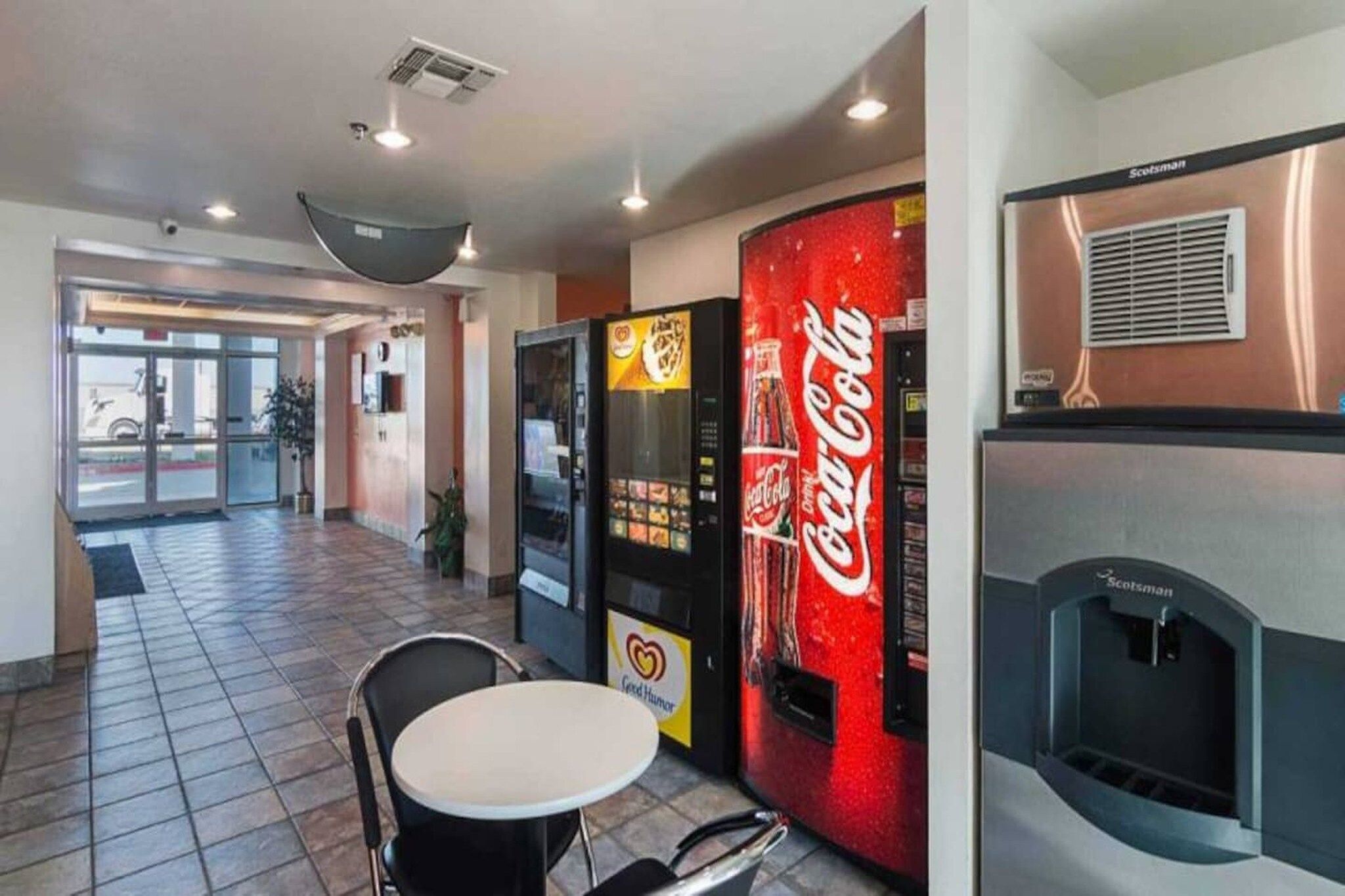 Un hall d’hôtel avec un distributeur automatique de Coca-Cola, un espace détente avec une table et des chaises, et une cheminée.