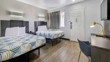 A hotel room with two beds, a desk, a chair, a lamp, and a door.