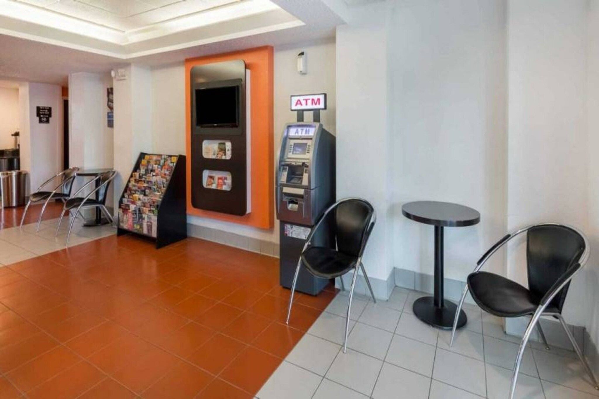 A lobby with an ATM, magazine rack, and two chairs.
