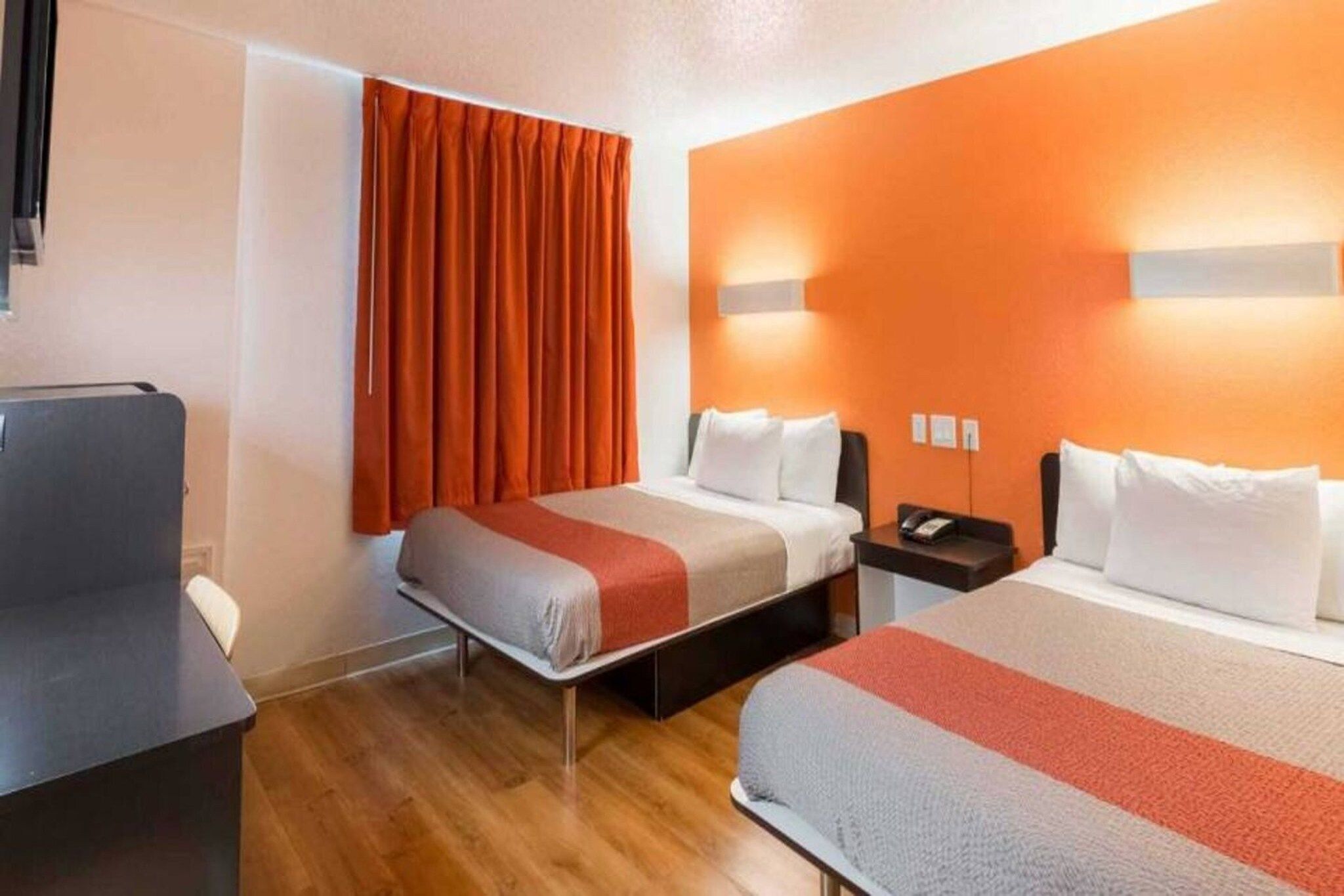 Una habitación de hotel con dos camas, un escritorio, una silla y una ventana con cortinas.