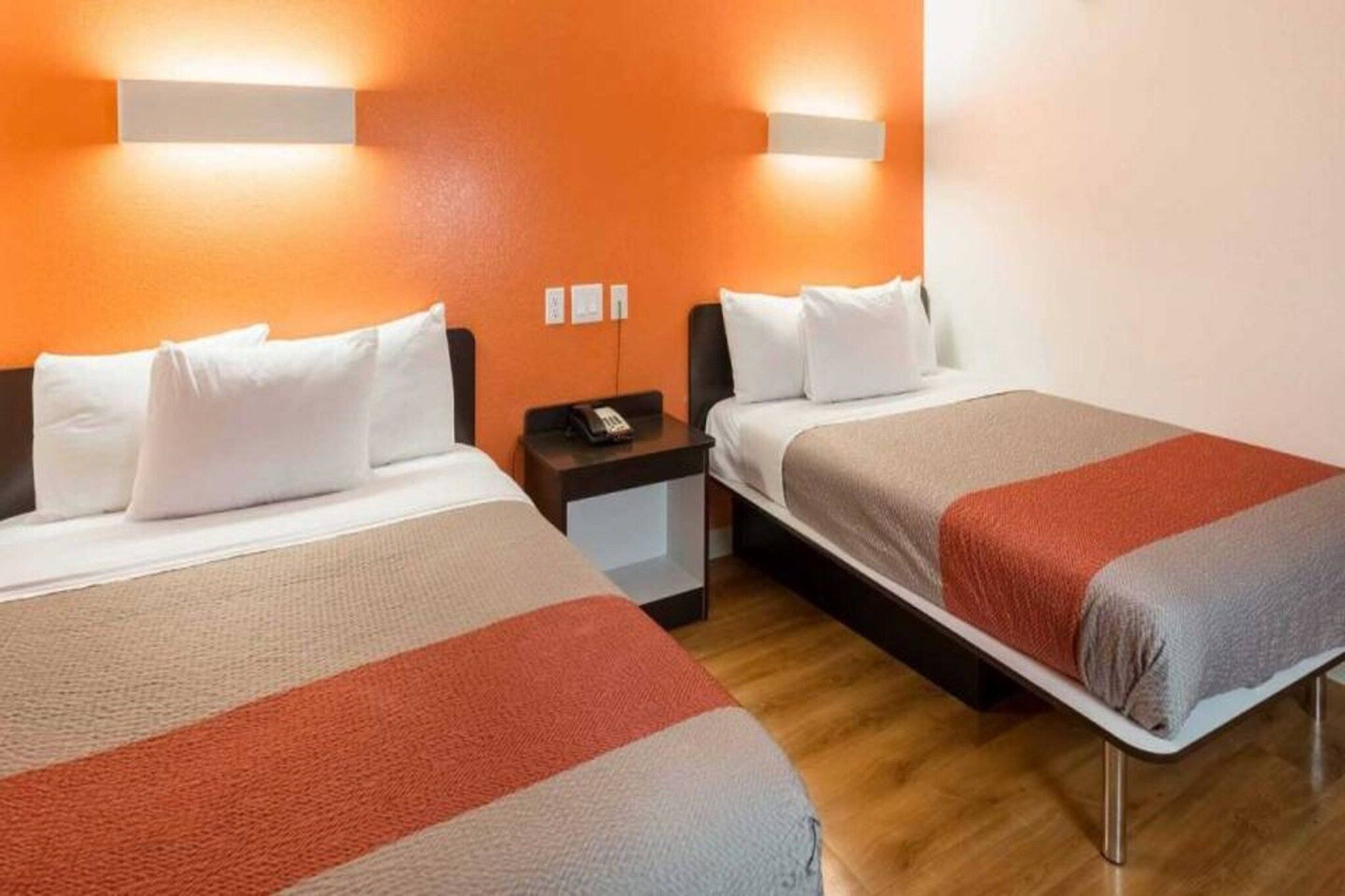 A hotel room with two beds, a nightstand, and a wall-mounted light fixture.