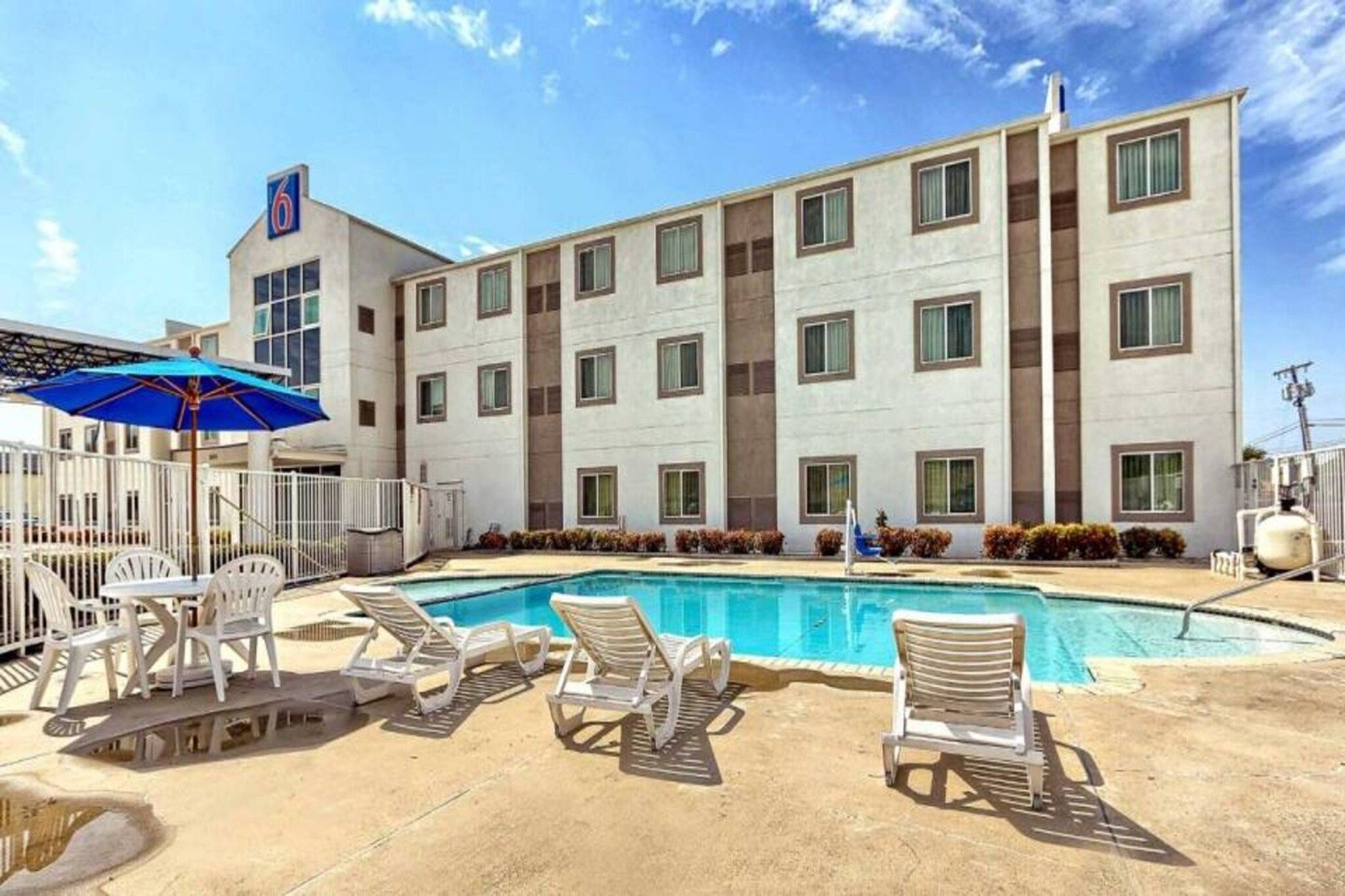 A hotel with a pool area, including lounge chairs and a blue umbrella.