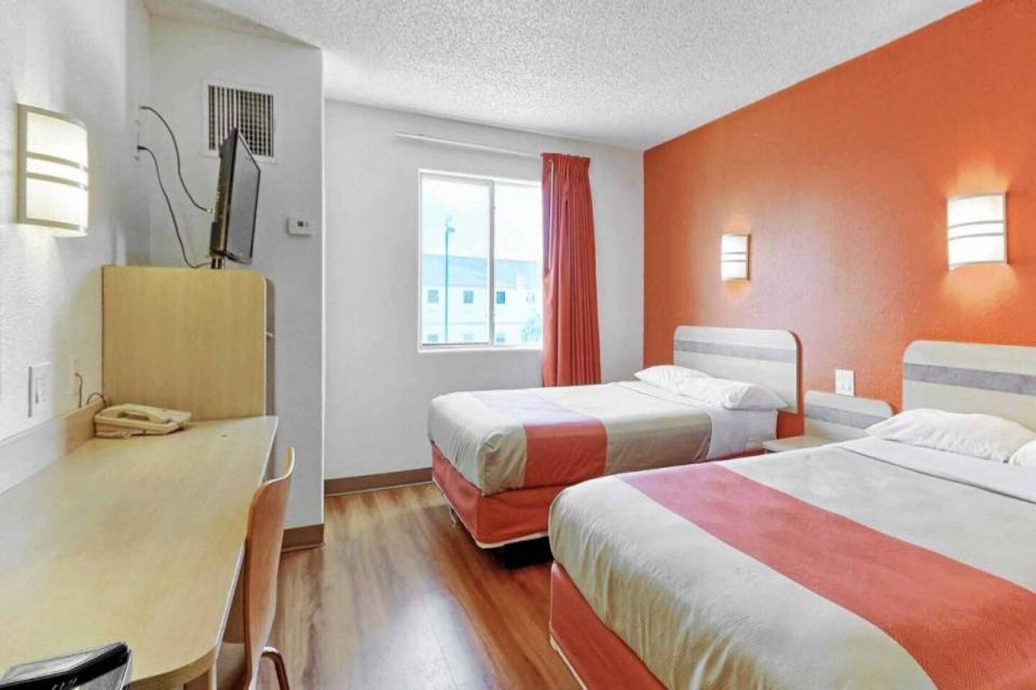 A hotel room with two beds, a desk, and a window with curtains.